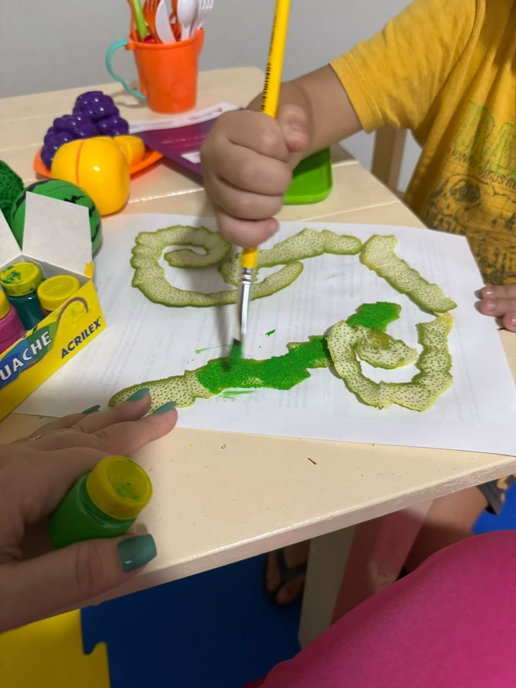 Mãos de criança pintando com casca de limão durante atividade de exploração de texturas