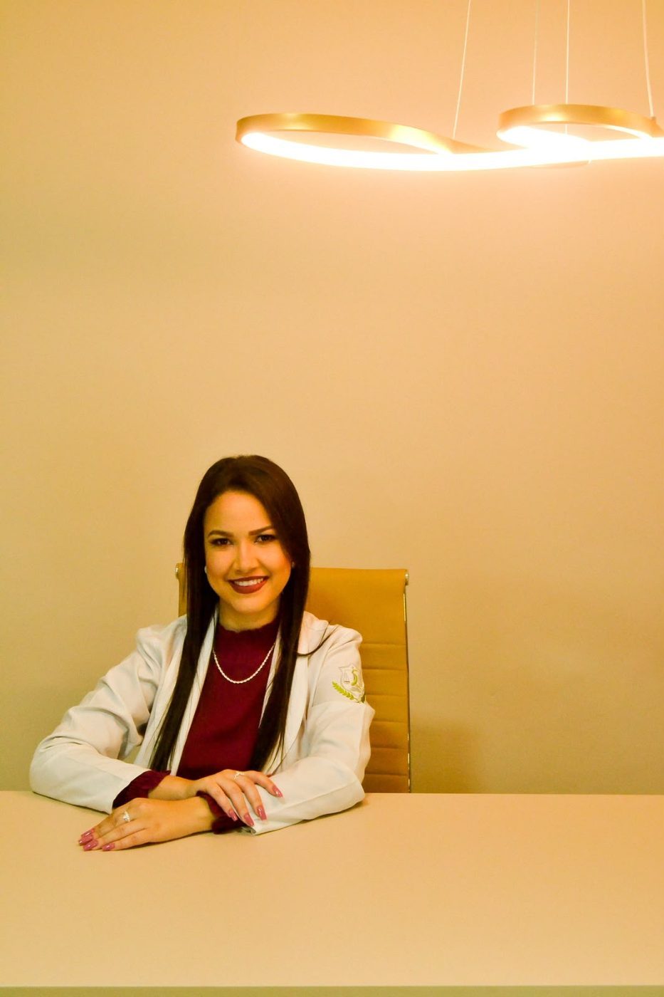 Jheniffer Rodrigues sentada à mesa do consultório, sob luminária